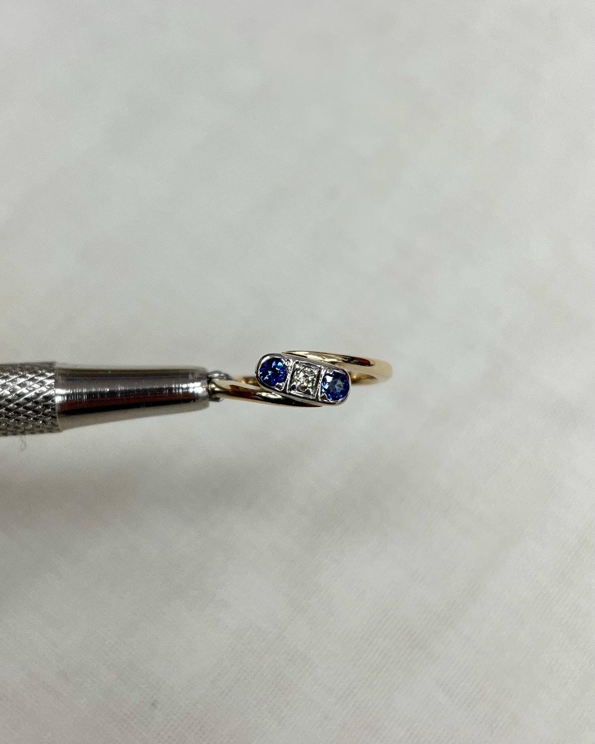 Gold ring with blue gemstones held by tweezers on a white background