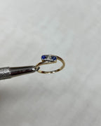 gold trilogy crossover ring with 2 blue sapphires and a diamond, held by metal tool above white background 