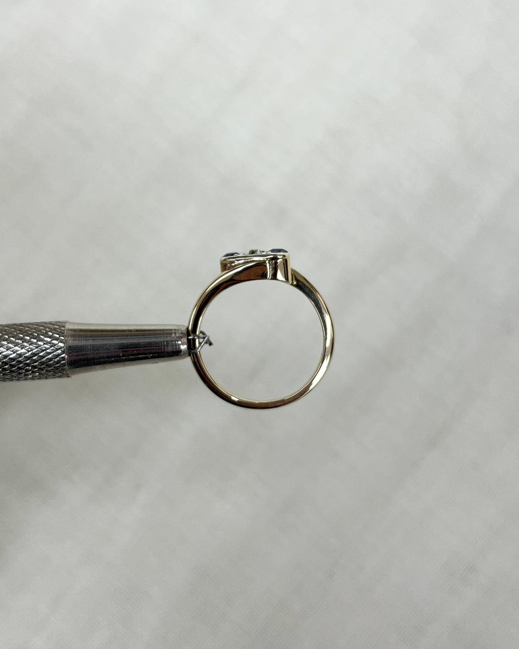 gold ring side view held by metal tool against white background 
