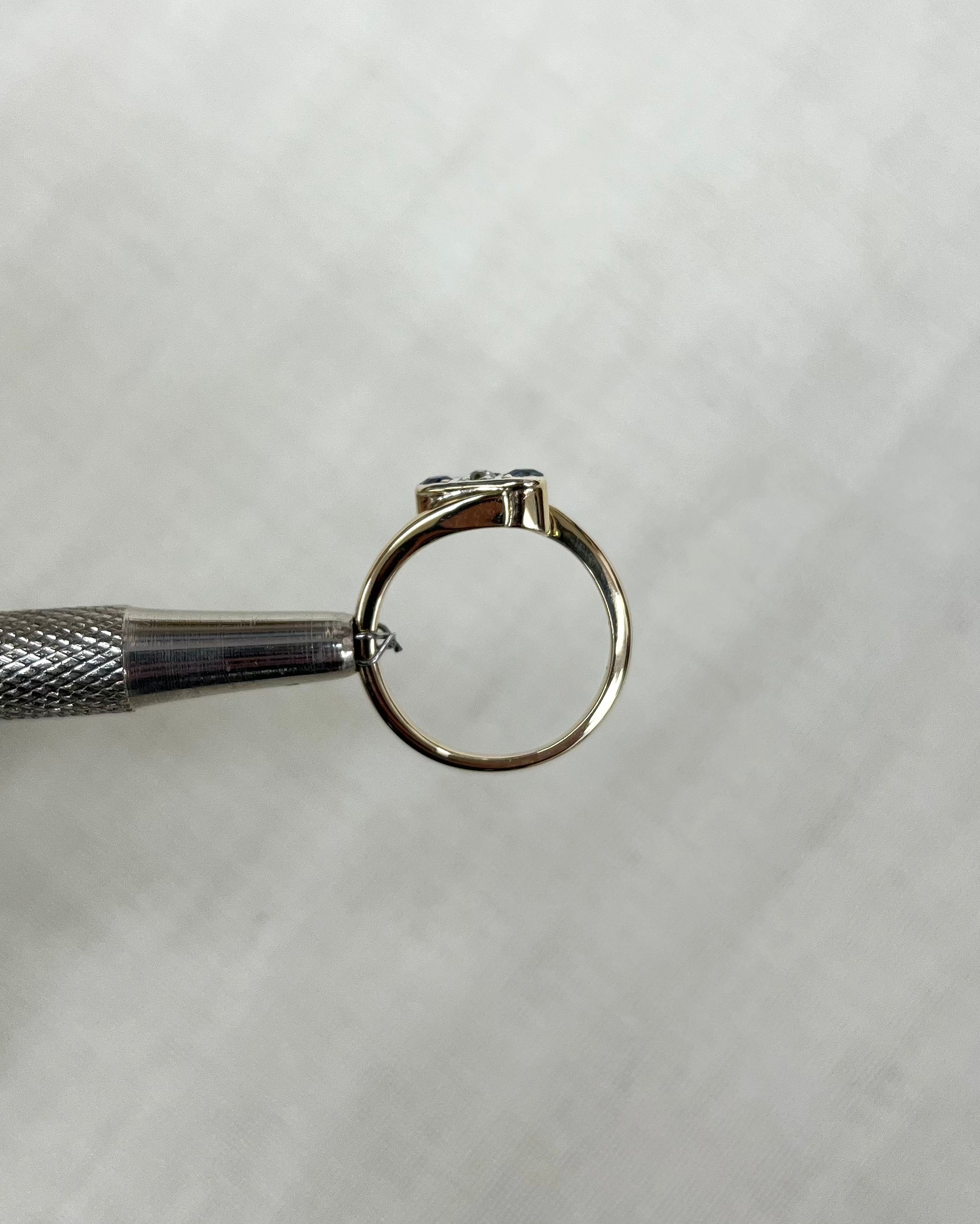 gold ring side view held by metal tool against white background 