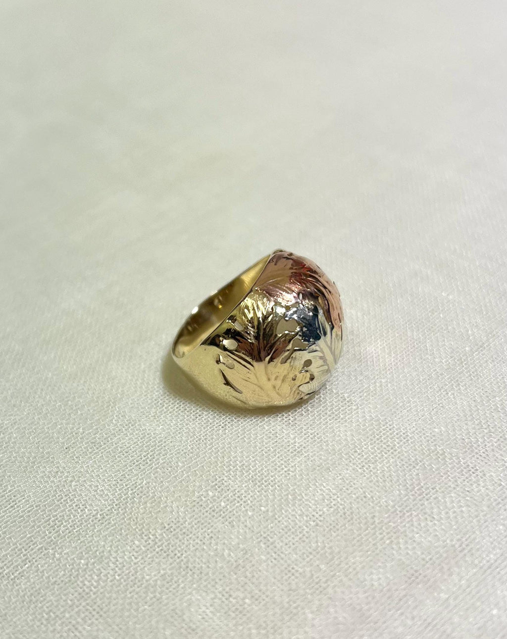 three tone gold ring with floral design on a white fabric background