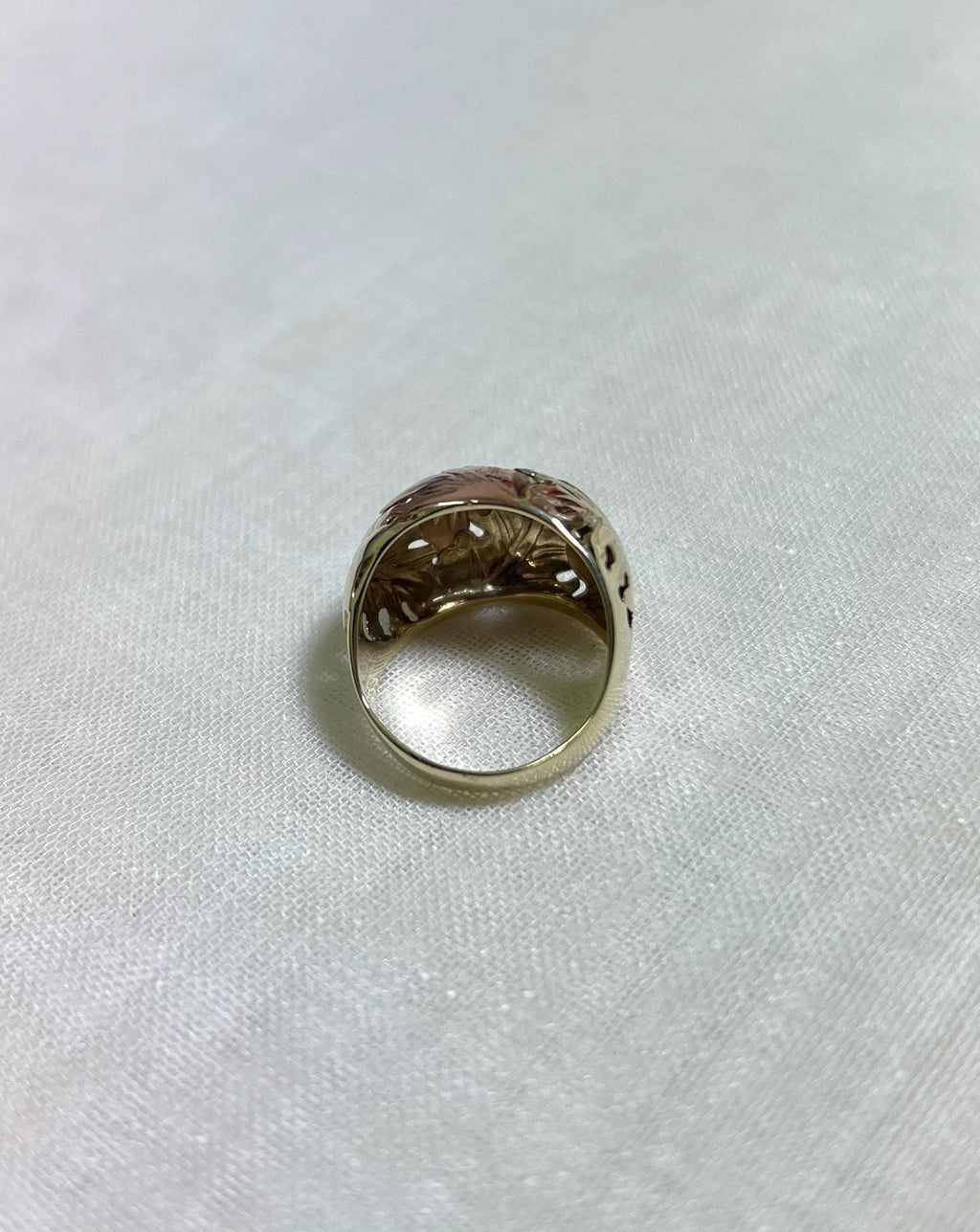back of gold ring with intricate design on a white fabric background