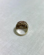 back of gold ring with intricate design on a white fabric background