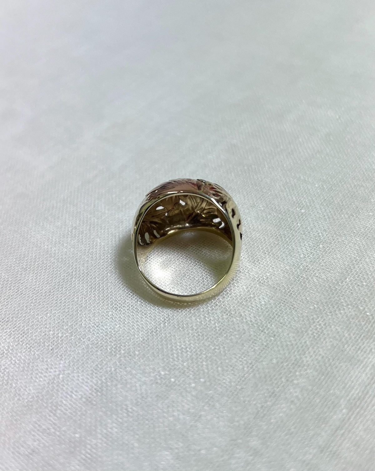 back of gold ring with intricate design on a white fabric background