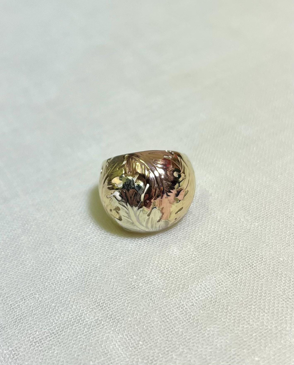 Gold ring with floral design on a white fabric background