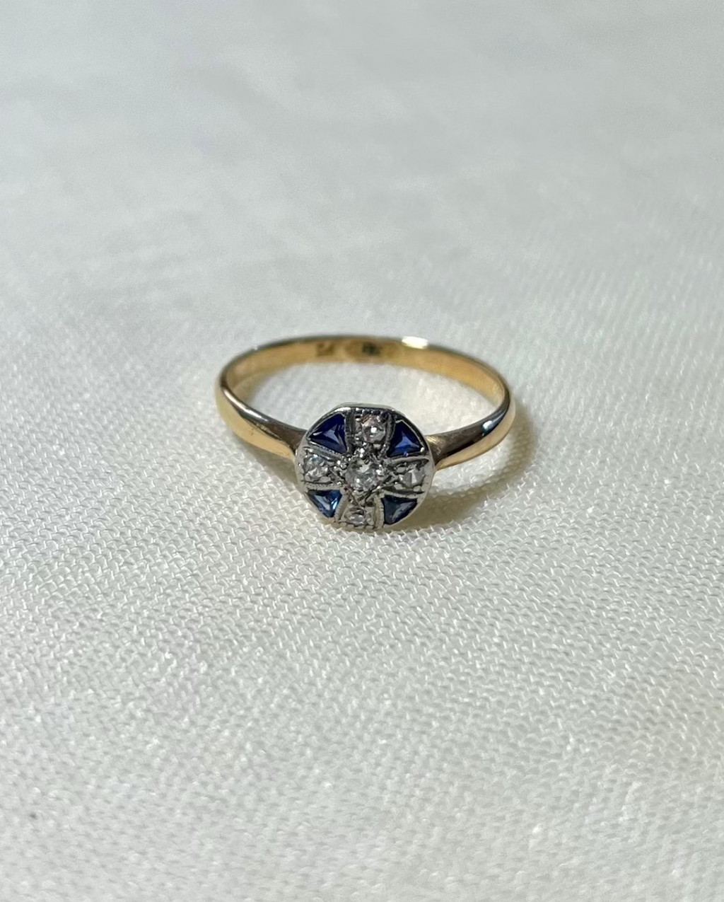 gold ring with circle head set with blue sapphire and diamond stones, resting on white fabric background 