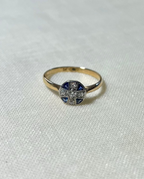 gold ring with circle head set with blue sapphire and diamond stones, resting on white fabric background 