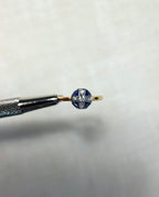 round gold ring with blue sapphire and diamond stones, held by silver tweezers above white background
