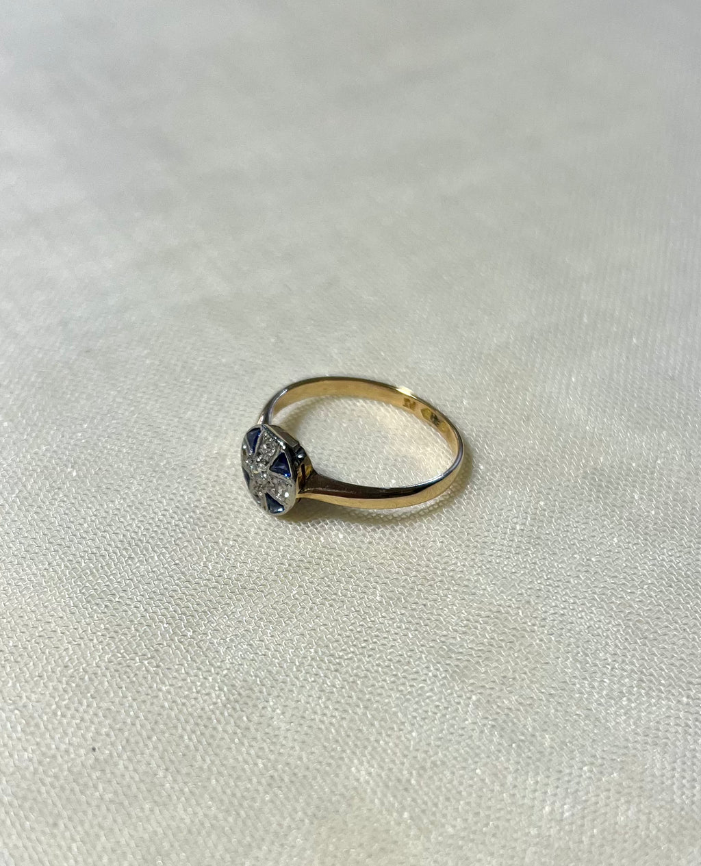 a yellow gold ring with blue sapphire and diamond cluster, resting on white fabric background