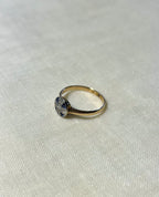 a yellow gold ring with blue sapphire and diamond cluster, resting on white fabric background