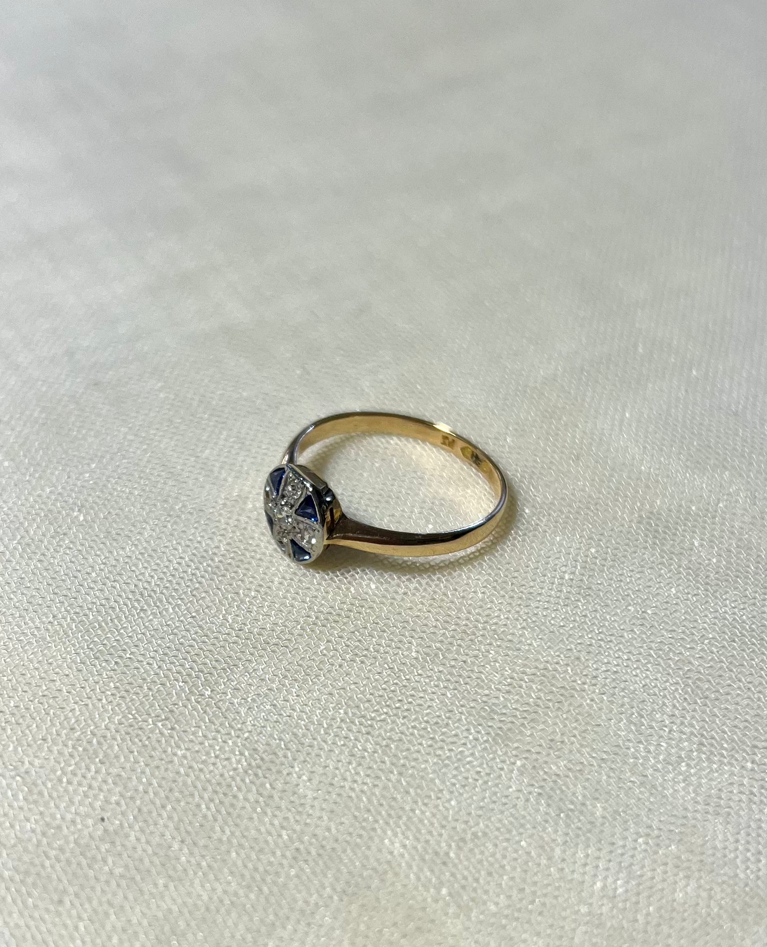 a yellow gold ring with blue sapphire and diamond cluster, resting on white fabric background