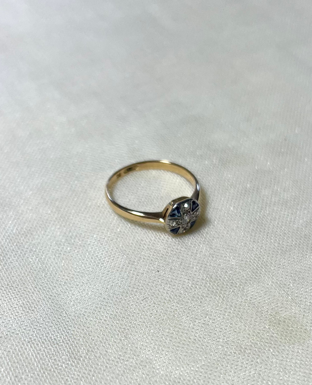 gold ring with sapphire and diamond cluster, on white fabric background 