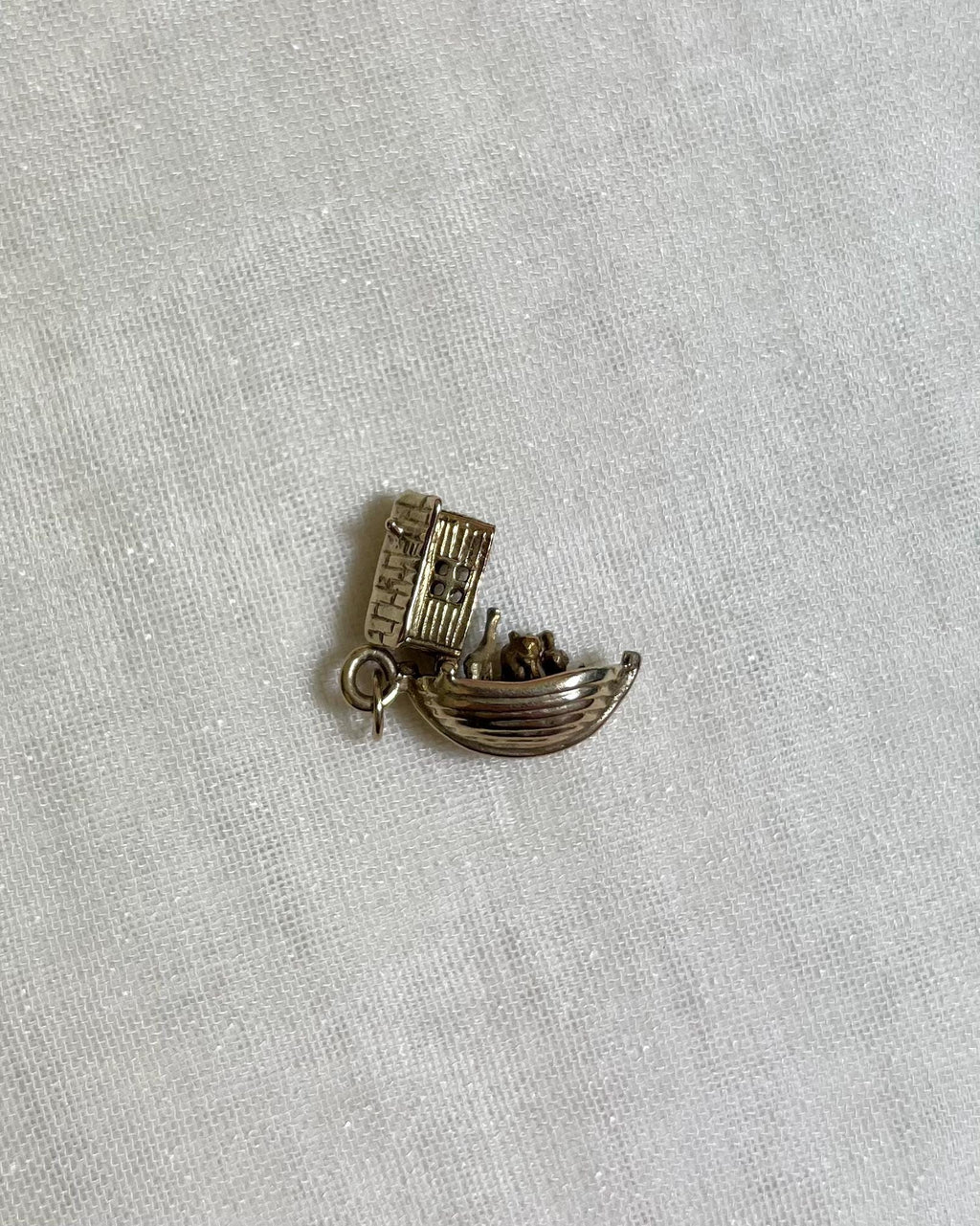 gold noahs ark charm open to reveal animals inside, on light fabric background 