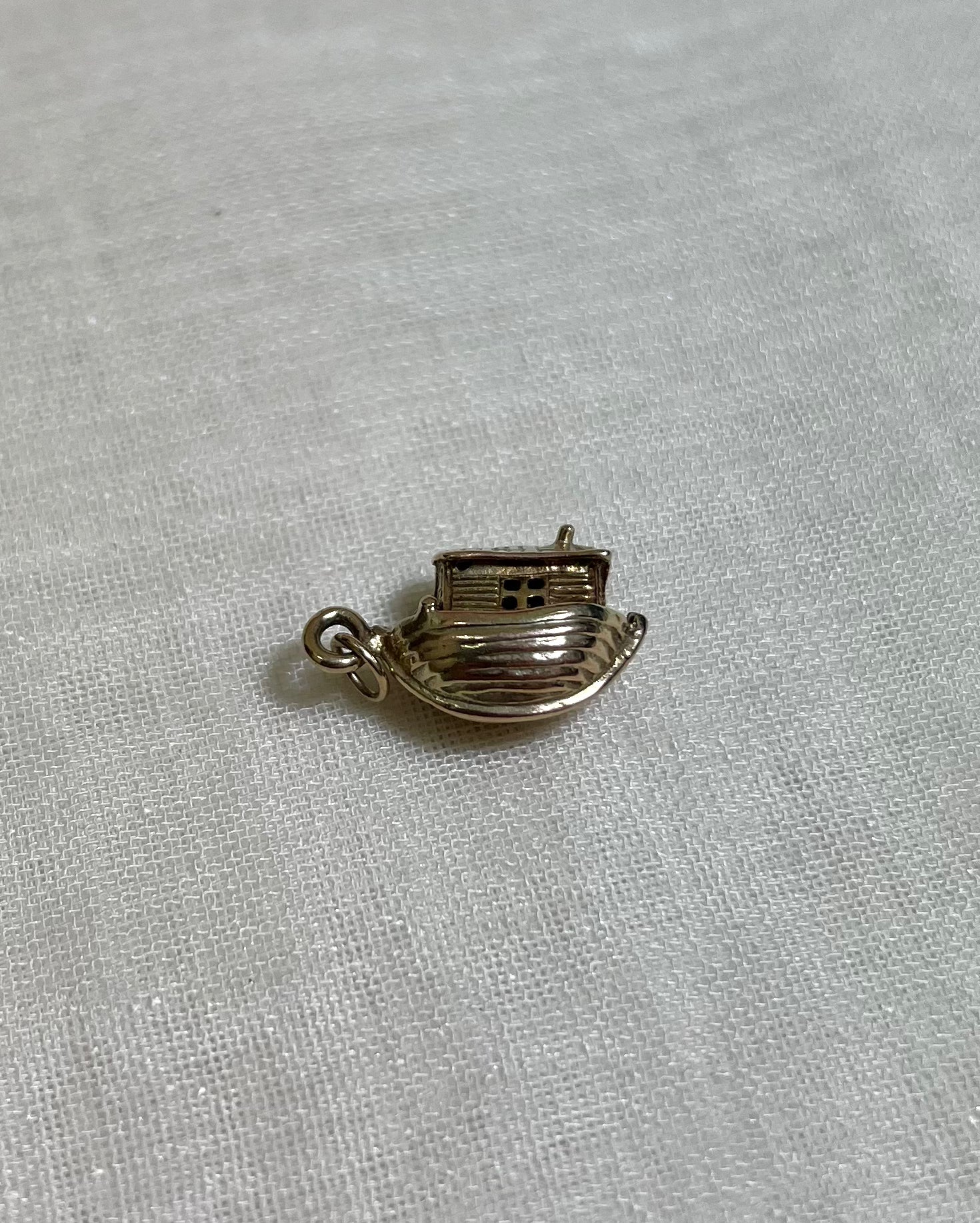 gold boat charm on light fabric background 