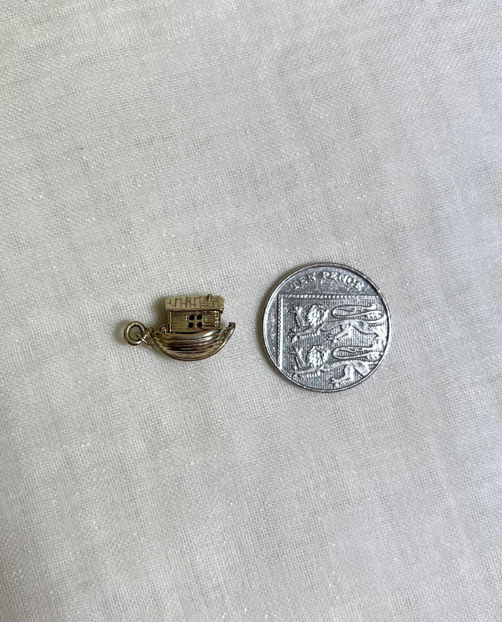 gold boat charm next to ten pence coin for size reference
