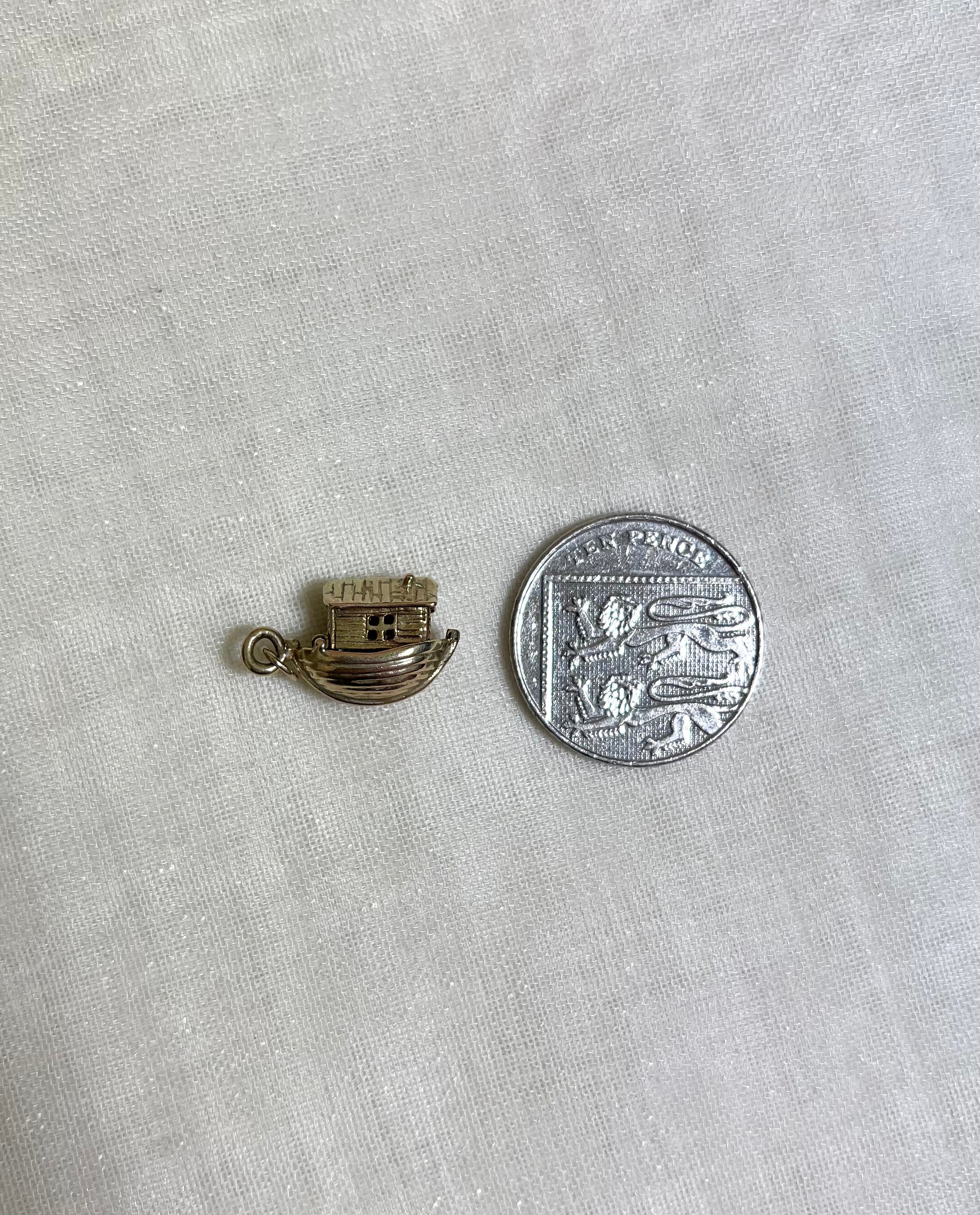 gold boat charm next to ten pence coin for size reference