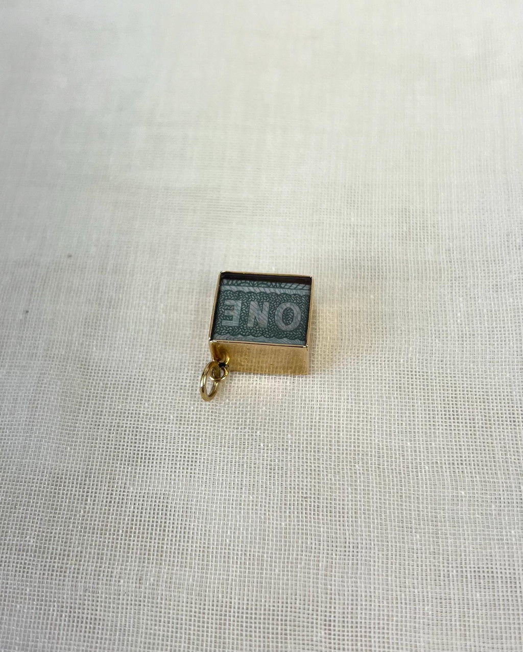 top side view of square gold charm with one pound note inside on white fabric background