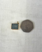 square gold charm with one pound note inside next to fifty pence coin for size reference, sitting on white fabric background.