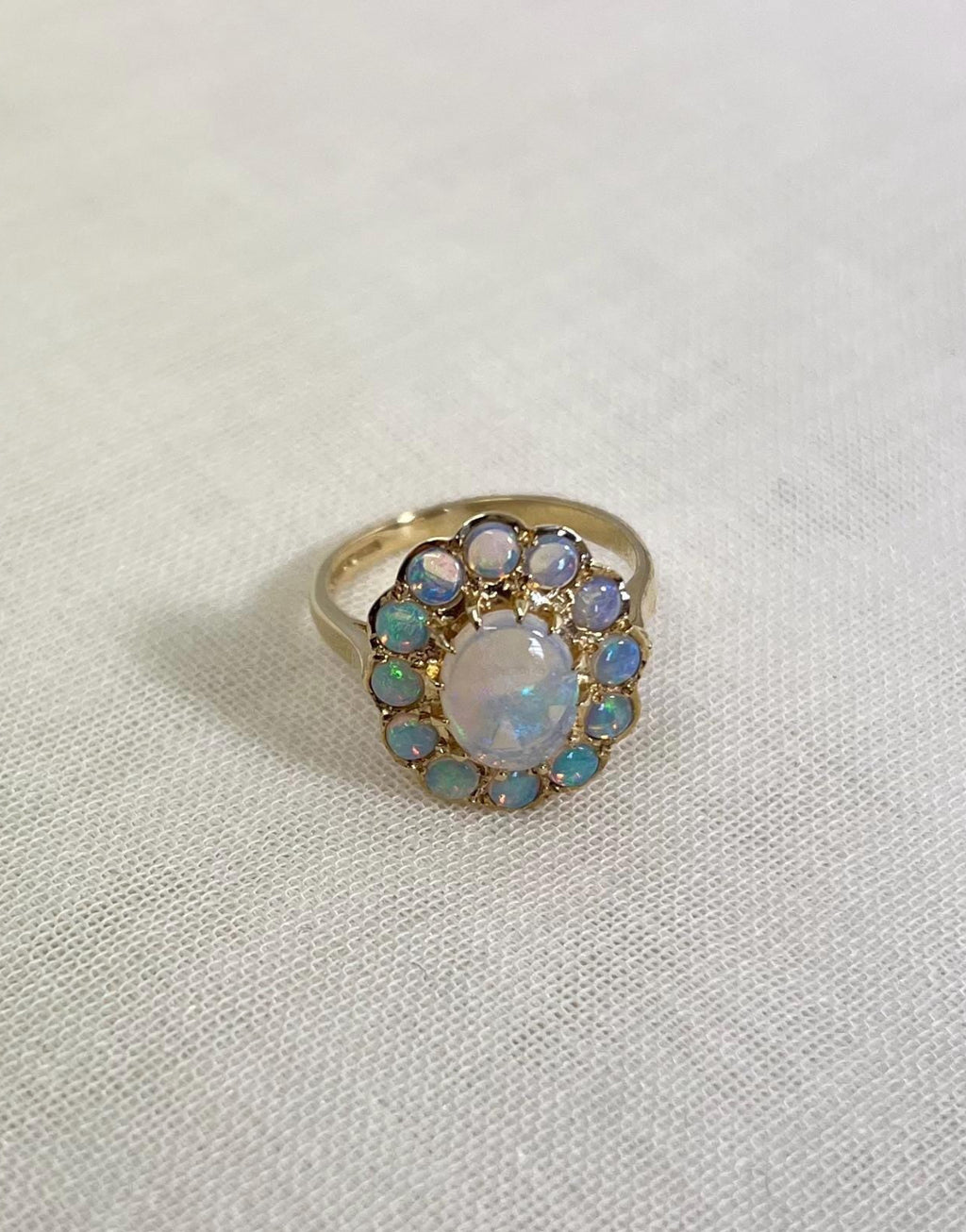gold ring with opal halo cluster, resting on white fabric background 