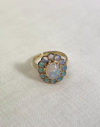 gold ring with opal halo cluster, resting on white fabric background 