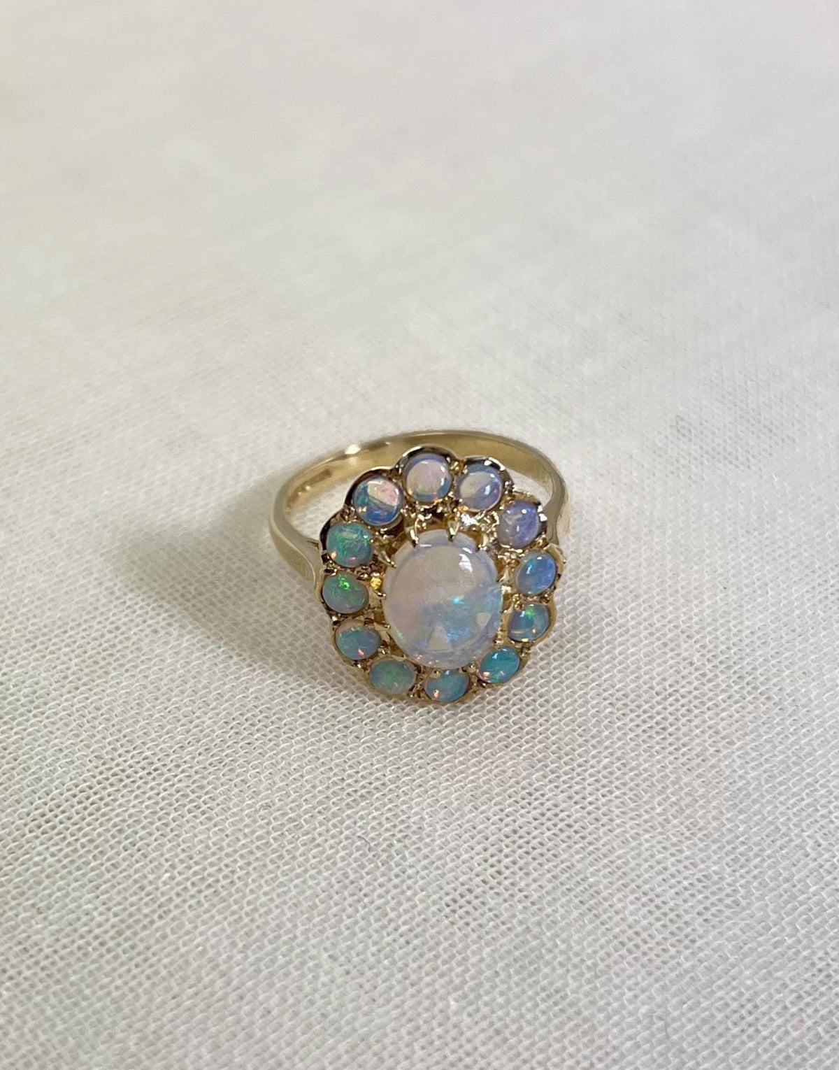 gold ring with opal halo cluster, resting on white fabric background 