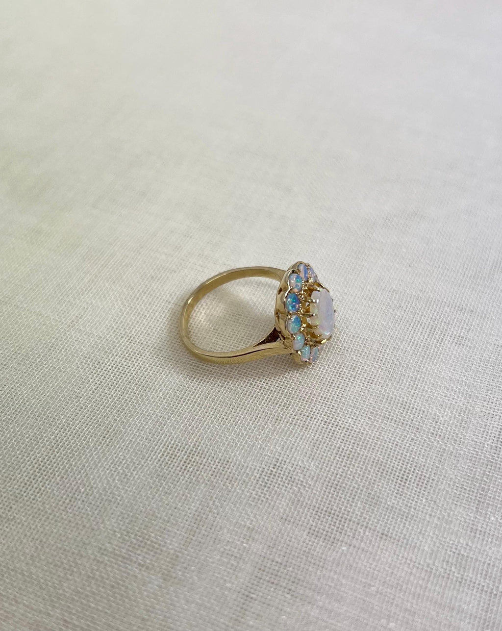 side view of gold ring with opal stones, resting on white fabric background 