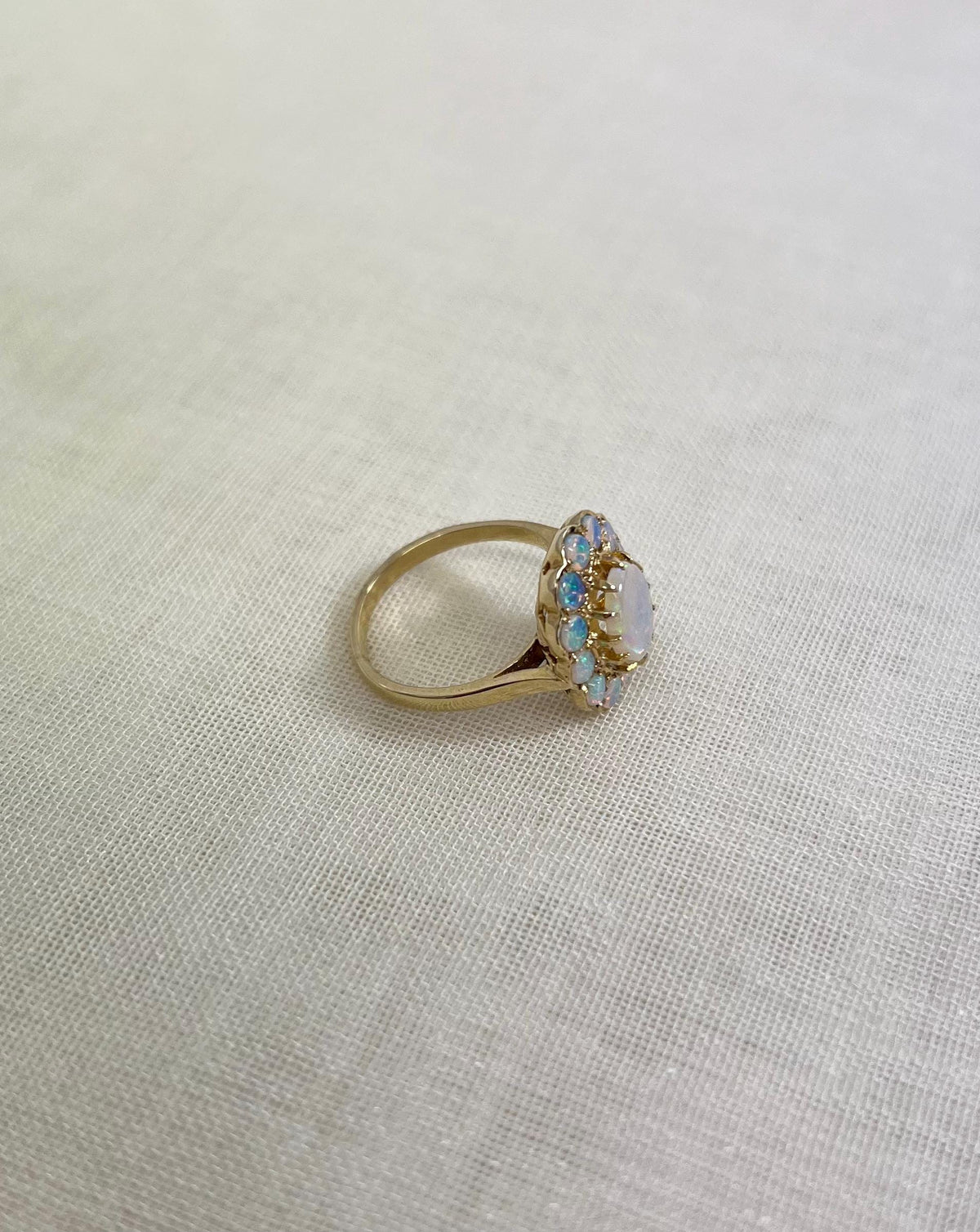side view of gold ring with opal stones, resting on white fabric background 
