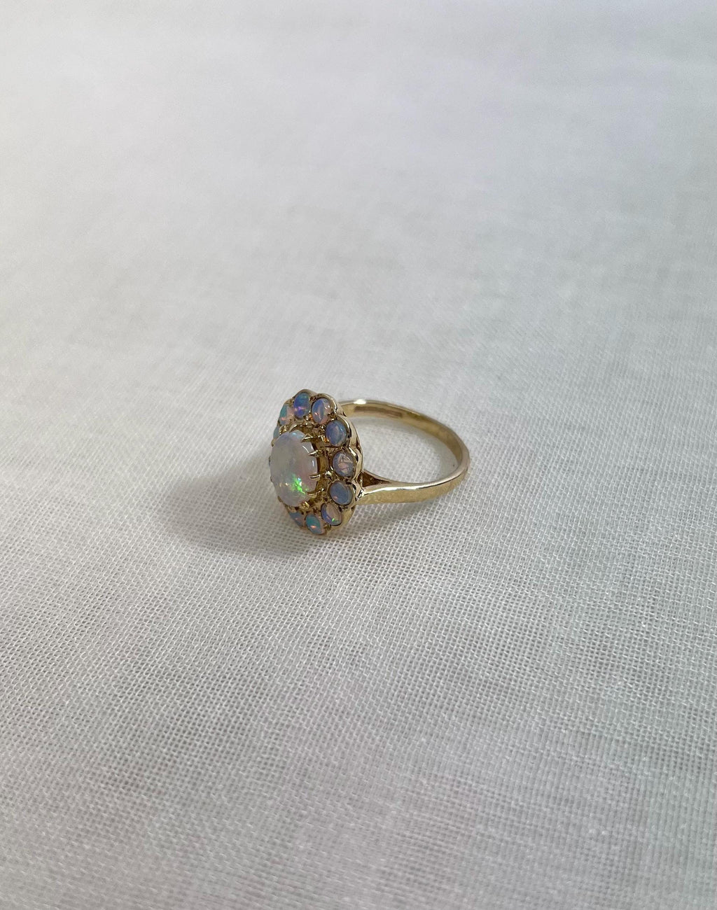 gold ring with opal halo cluster, resting on white fabric background