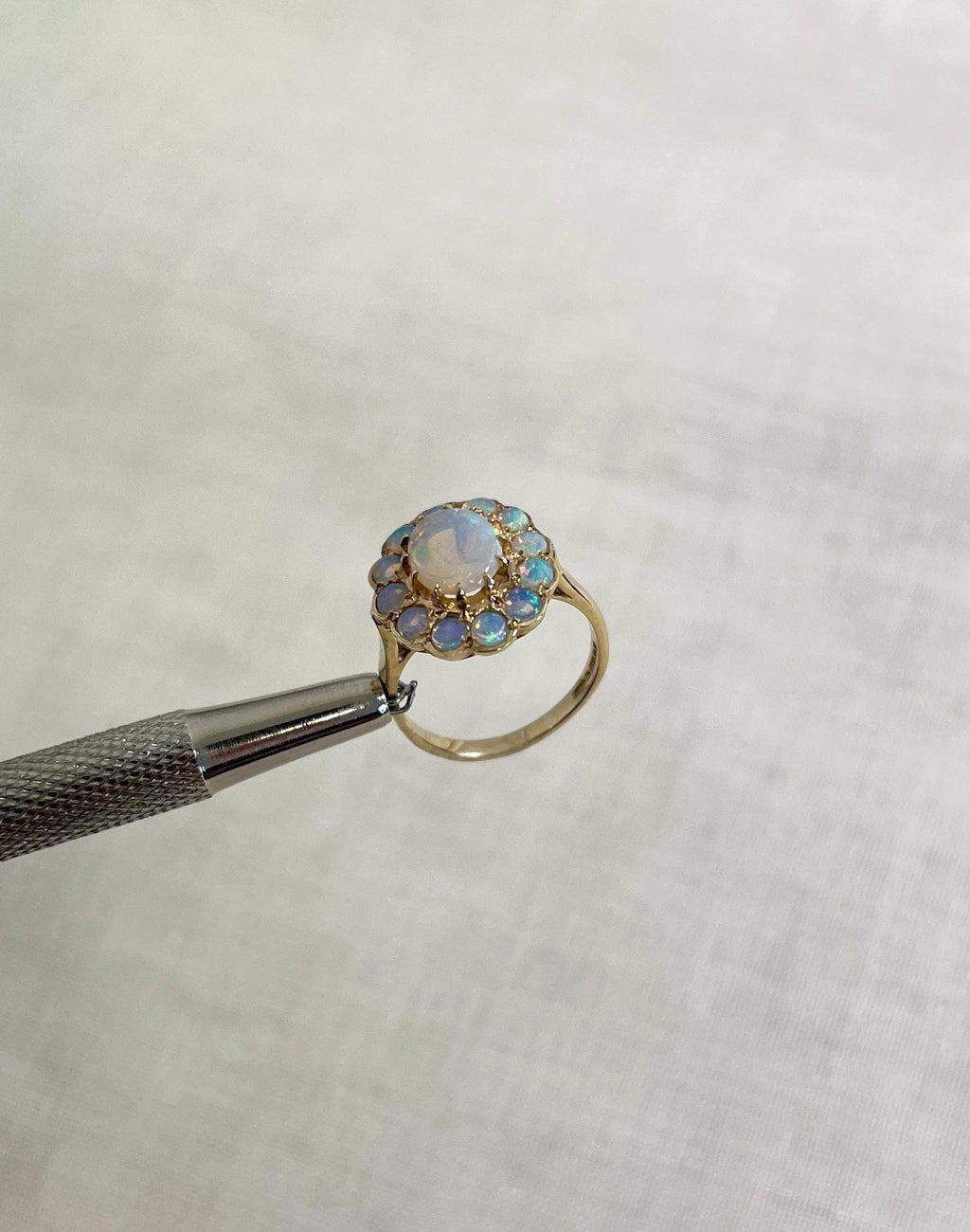 Gold ring with opal stones held by tweezers on a white background