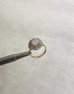 Gold ring with opal stones held by tweezers on a white background