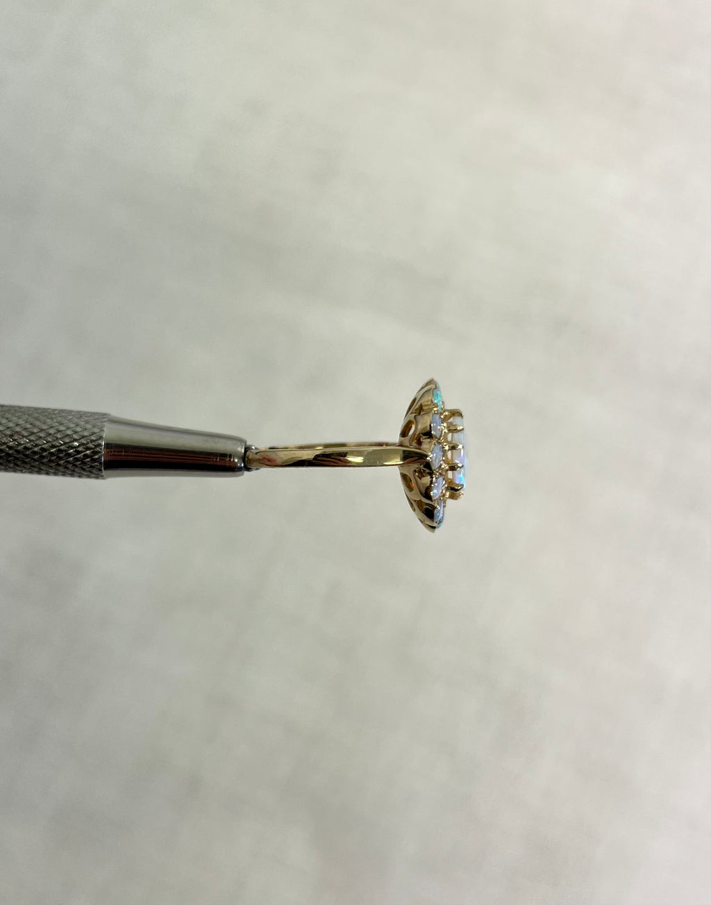 side view of gold ring with opal stones, help by silver metal tool on white background.