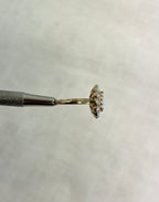 side view of gold ring with opal stones, help by silver metal tool on white background.