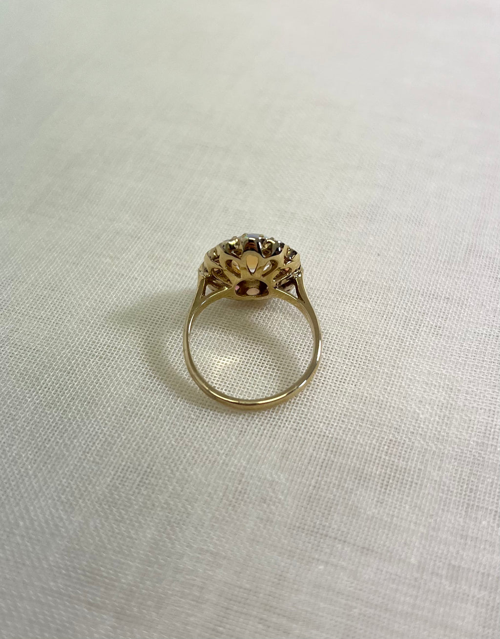 back view of gold ring, resting on white fabric background.