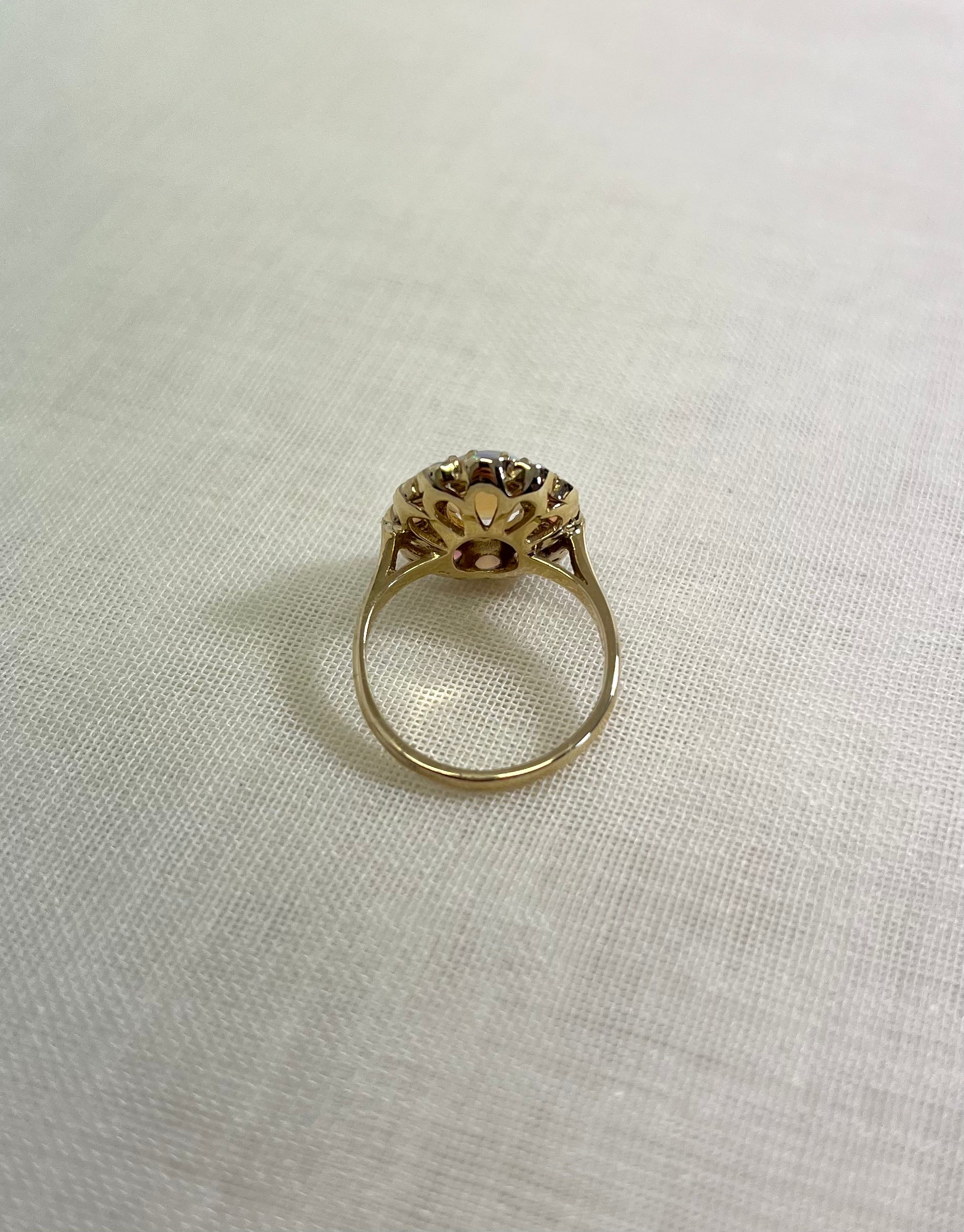 back view of gold ring, resting on white fabric background.