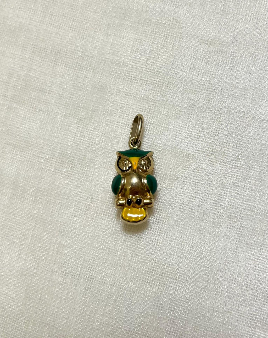 Gold owl charm with green and yellow accents on a light cream fabric background