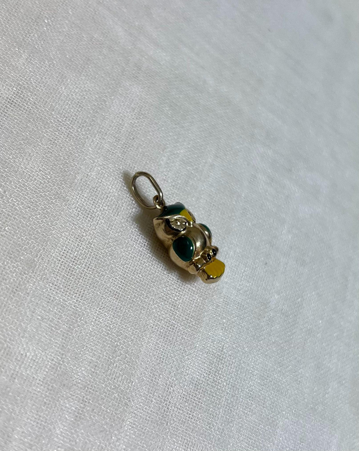 gold owl charm with green and yellow enamel accents on light cream fabric background
