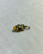 gold owl charm with green and yellow enamel accents on light cream fabric background