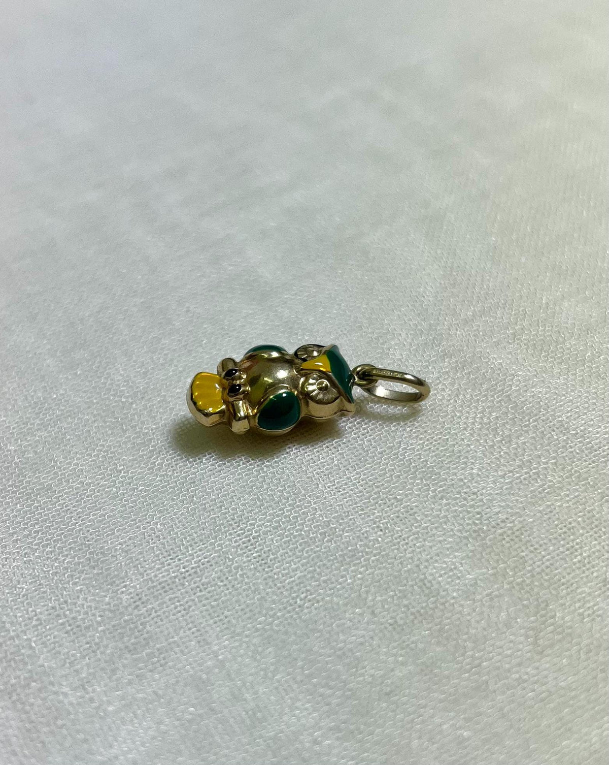 gold owl charm with green and yellow enamel accents on light cream fabric background