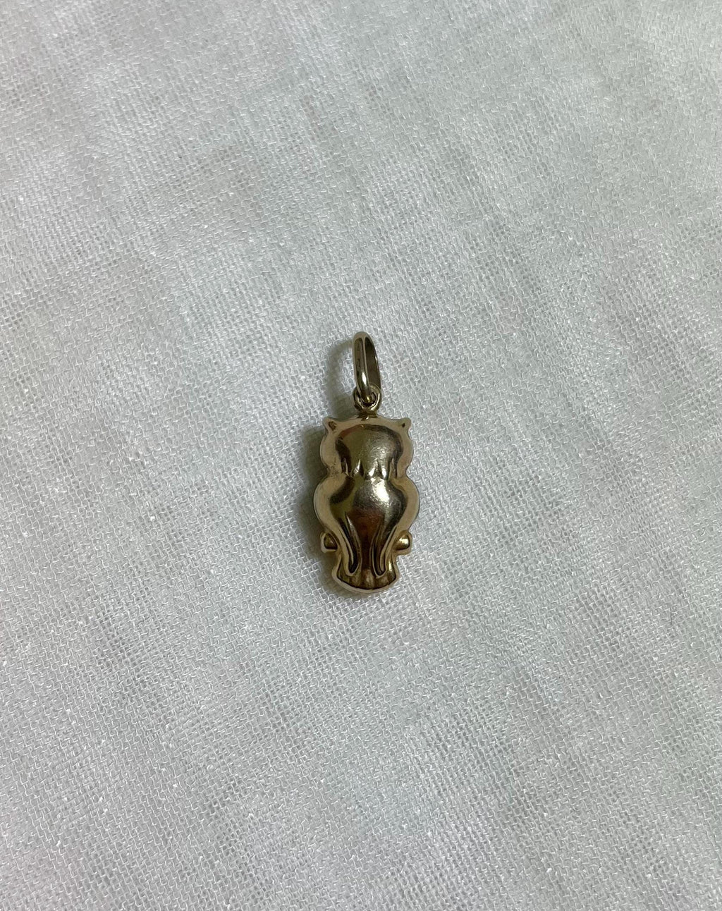 back of gold owl charm on light cream fabric background 