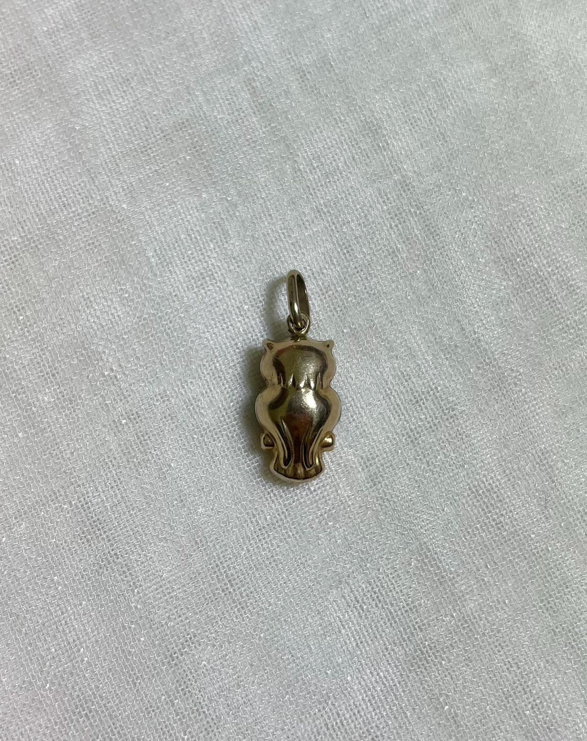 back of gold owl charm on light cream fabric background 