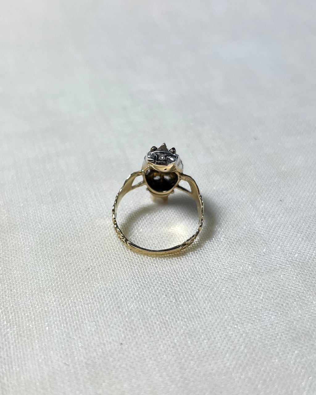 back view of gold stone set ring, on white fabric background