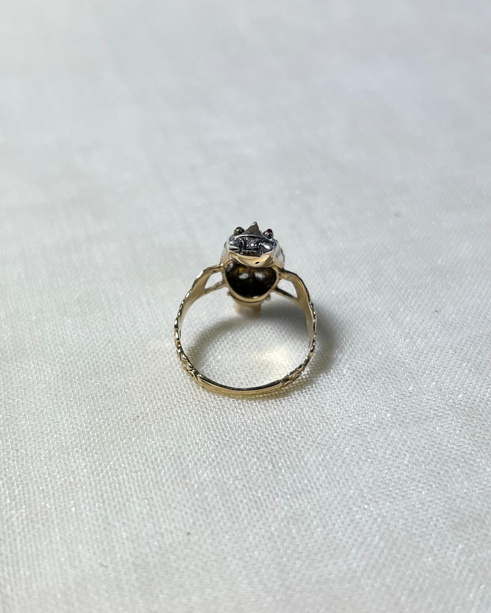 back view of gold stone set ring, on white fabric background