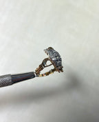 side view of bird shaped ring set with diamonds, held by silver metal tool against soft white background