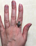 A close-up of a person's hand wearing a vintage owl-shaped ring. The ring features diamond set body and gold band, set against a plain light beige background.