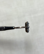 side view of gold ring held by silver metal tool above soft white background
