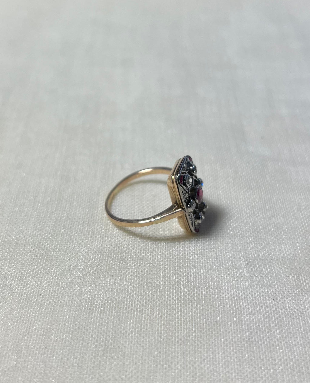side view of vintage style gold ring set with pink rubies and diamonds, resting on white fabric background