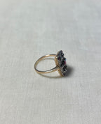 side view of vintage style gold ring set with pink rubies and diamonds, resting on white fabric background