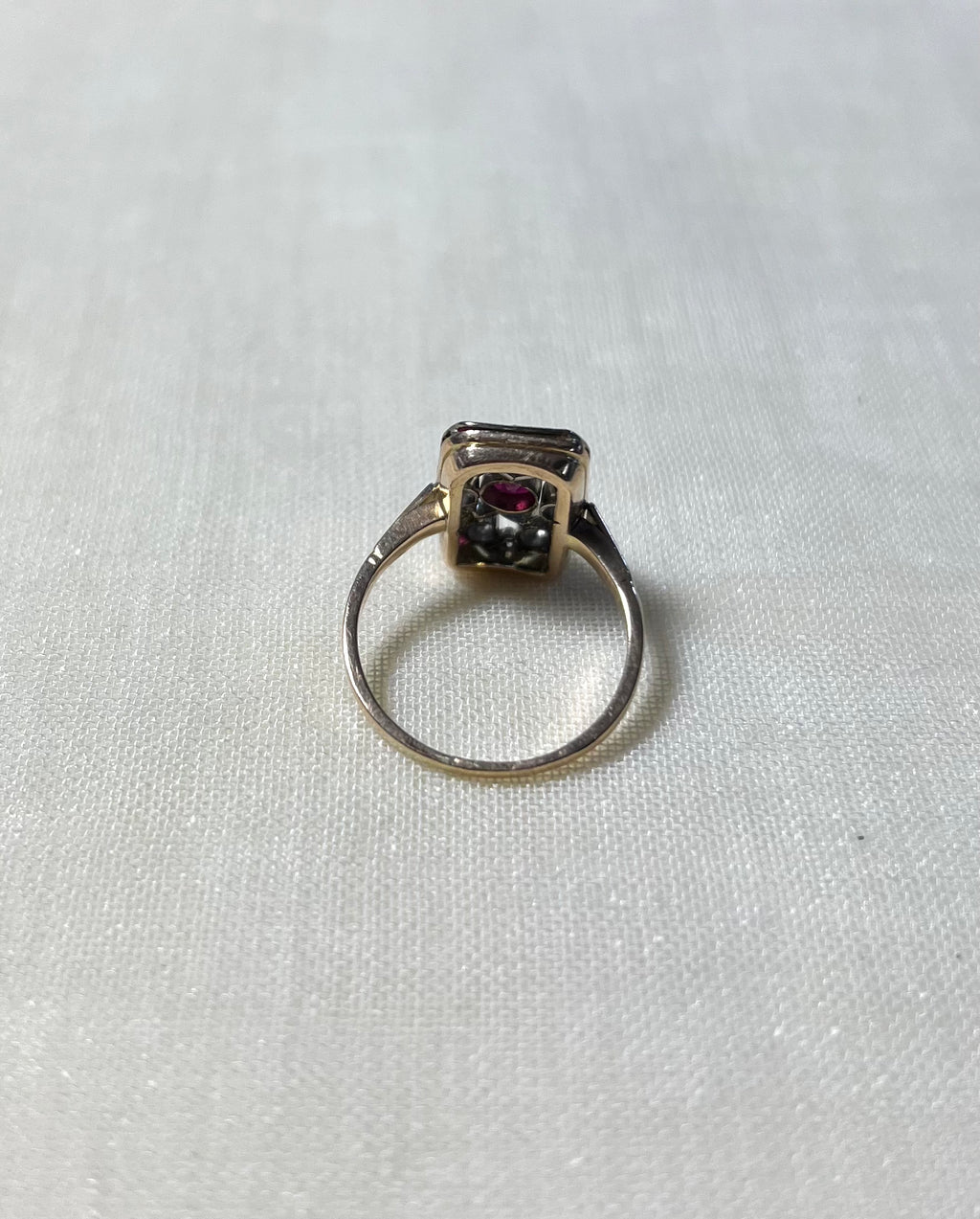 back view of rectangular gold ring, resting on white fabric background