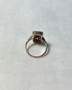 back view of rectangular gold ring, resting on white fabric background