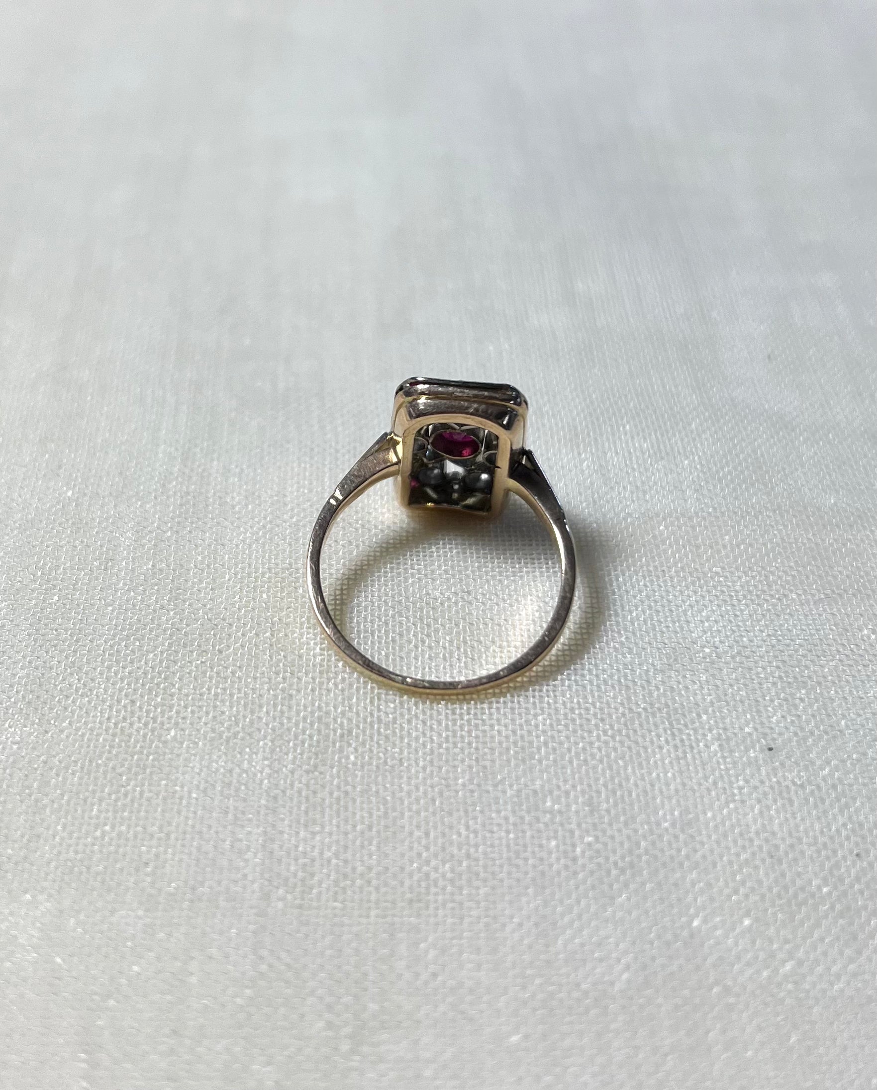 back view of rectangular gold ring, resting on white fabric background